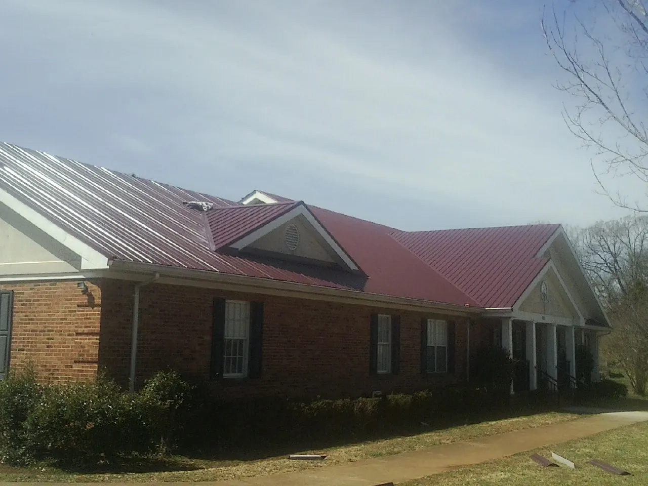Red metal roof with gabled entries on a long brick building, from a Hail Damage Roof Repair job in Talladega