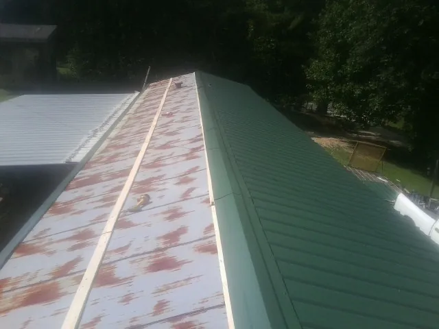Old rusted panels beside newly installed green metal roofing — Wind Damage Roof Repair by Roofing Brothers in Talladega