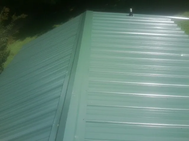 New green metal panels meeting at the ridge of a roof — Flat Roof Repair work by our crew in Talladega