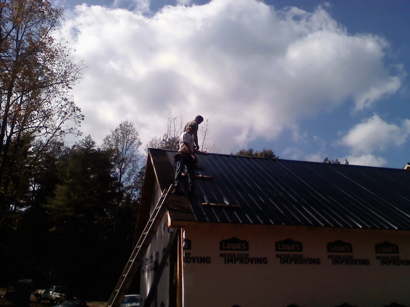 Roofer fastening dark metal panels high against a cloudy sky, from a Roof Inspection job in Talladega