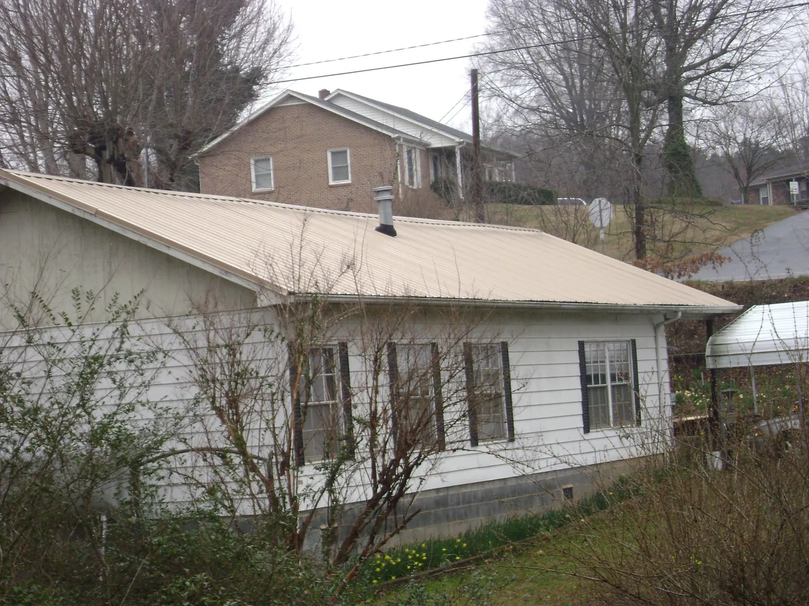 Tan metal roof on a white sided house set into a hillside — Commercial Roofing by Roofing Brothers in Talladega