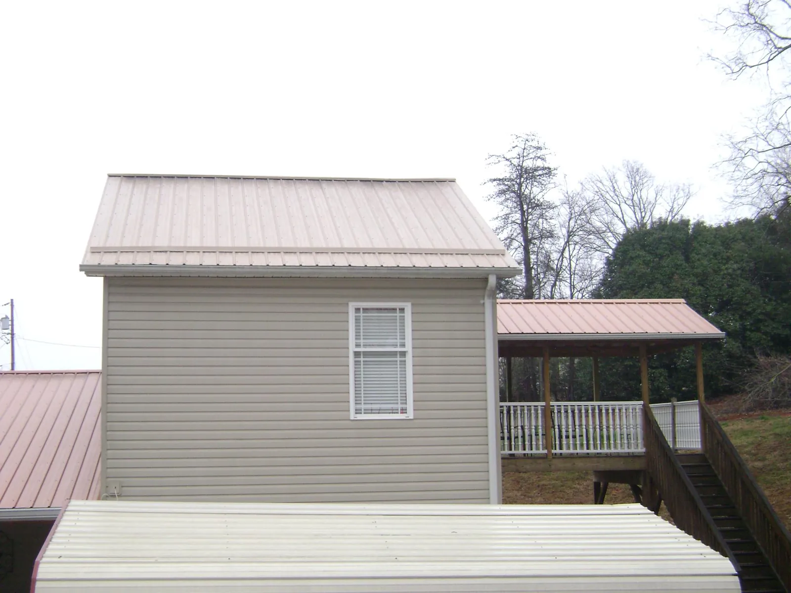 Tan metal roofs on a two story addition and attached porch, from a Roof Replacement job in Talladega
