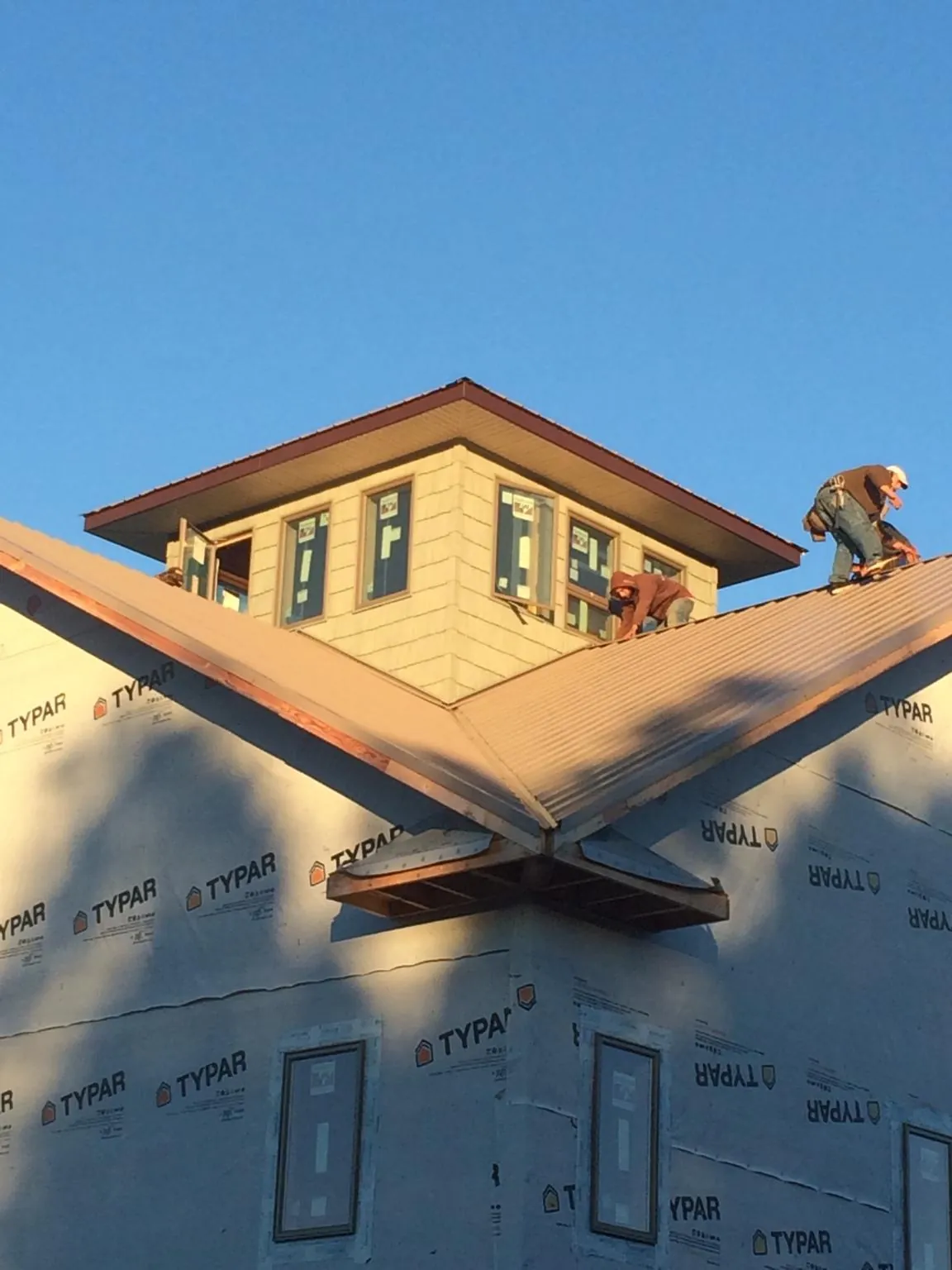Roofers working around a rooftop cupola on a new metal roof at sunset — Roof Waterproofing in Talladega by Roofing Brothers